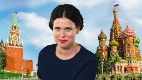 A girl smiling sat in front of a picture of Russia.