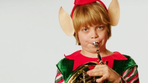A boy in an elf costume playing a brass instrument.