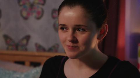 A girl sat in her bedroom looking happy, Chloe from The Dumping Ground.
