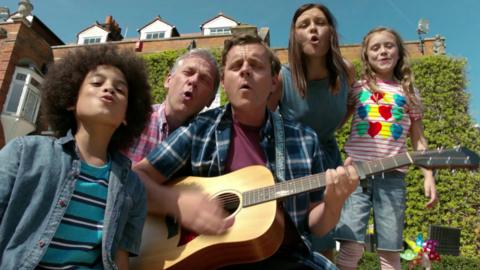 Simon is on the guitar surrounded by the family who are all howling.