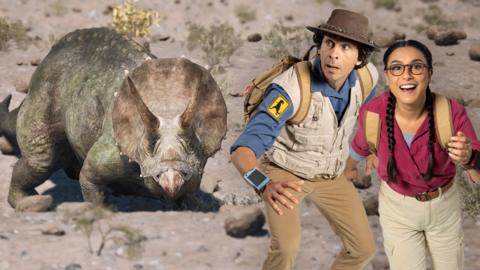 Andy and Jen are stood on the right-hand side of a triceratops in a desert.