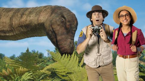 Andy and Jen pose next to a dinosaur with a long neck looking down at them both.