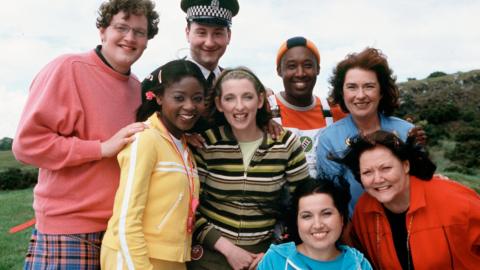 Image of the original Balamory cast smiling in front of the camera.
