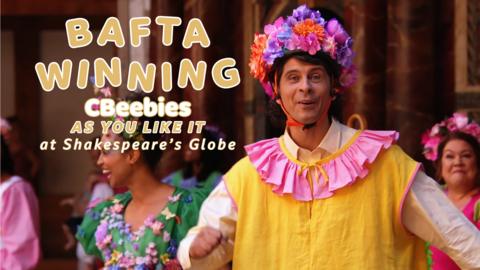 Andy Day in stage dress up wearing a bright yellow top and pink flowery head band.