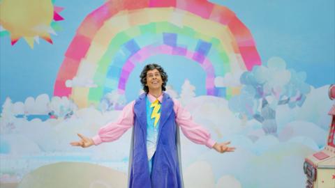 Professor Raindrop standing with his arms out, beaming under a bright rainbow.