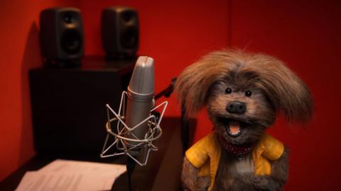 Dodge in a radio studio with a microphone