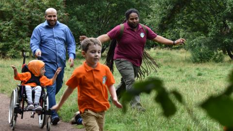 Image of children and adults walking through a forest with Ranger Hamza.