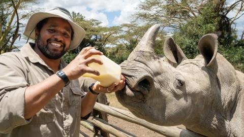 Hamza feeds a baby rhino with a huge bottle of milk.