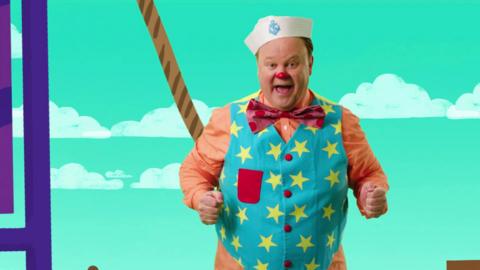 Mr Tumble is wearing a blue waistcoat with yellow stars, and has a sailors hat on.