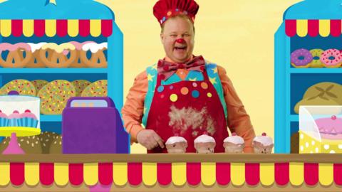 Mr tumble is dressed as a chef with current buns in front of him.