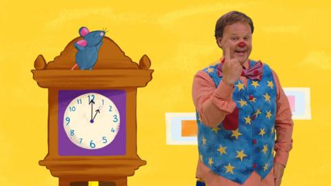 Mr Tumble and a mouse sat on top of a clock
