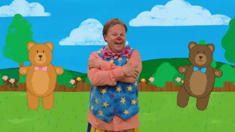 Mr Tumble with two teddy bears in a garden