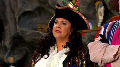 Captain Captain, a woman with a pirate hat on is looking serious.