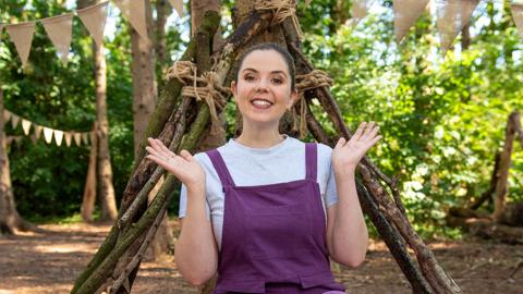 Lisa from Tiny Tunes in a wood with bunting and a homemade shelter behind her.