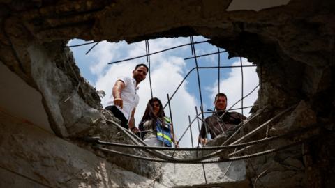 People survey damage to a building in Israel following a Hezbollah rocket and drone attack (25 August 2024)