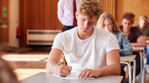 GCSE Biology image: an exam hall with teenage students taking exams, concentrating, male student in the foreground.