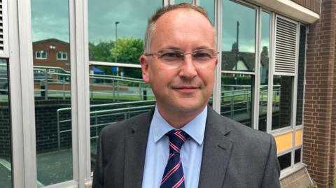 Jonathan Lester, council leader, standing outside the authority's offices and wearing a grey suit with a shirt and tie.