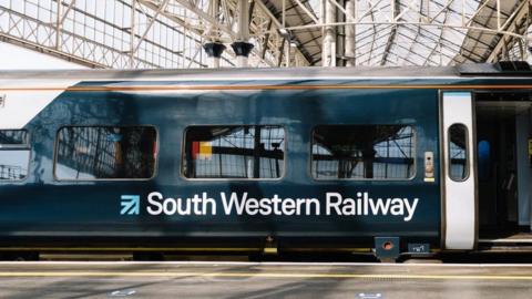 Train with door open stopped on platform with white ironwork roof of railway station above and behind