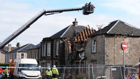 Police tape in front of the street where a house exploded in Alloa - the ruined house can be seen behind the tape