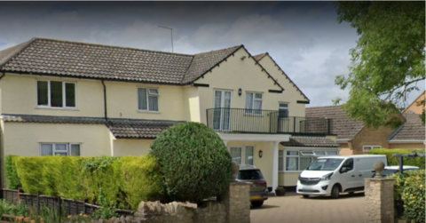 A two storey yellow building with a black iron balcony on the front of the property. A white van is parked outside.