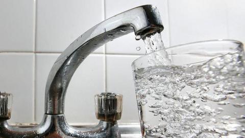 A silver coloured sink beside a glass full of water