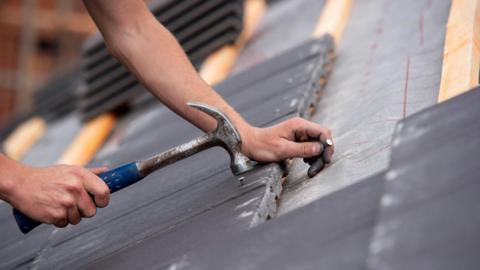 Stock image of person fixing a roof with hammer