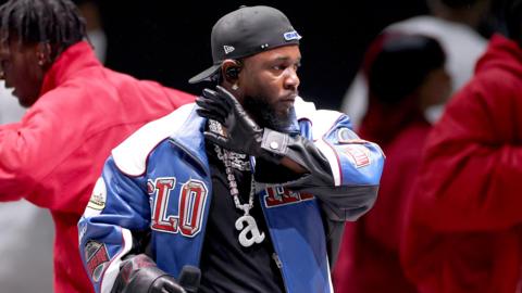 Kendrick Lamar performing at the Super Bowl, wearing a cap and gloves and a silver chain