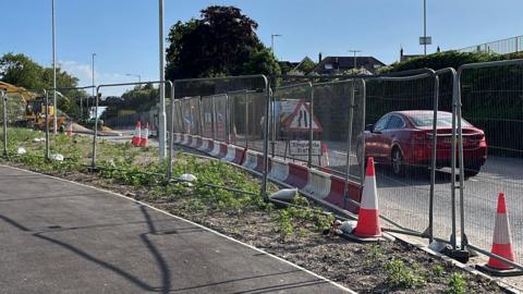 An image of a road. It is lined by traffic cones and metal fencing. 