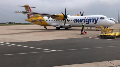 A yellow and white plane with the word Aurigny on the side of the fuselage. 