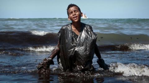 Boy walks out of the sea covered in oil