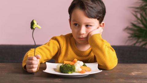 Young boy looking skeptically at vegetables on his plate 