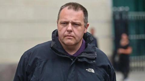 Neil Beckett leaving court wearing a black North Face rain jacket and a purple top.