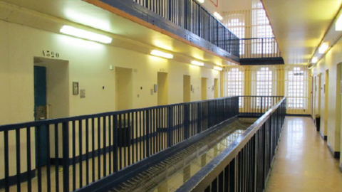The inside of a prison with cream walls and black metal bars.