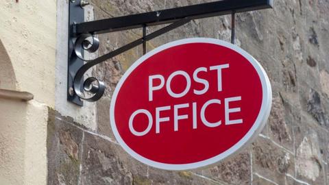 A red oval Post Office sign attached to a brick wall.