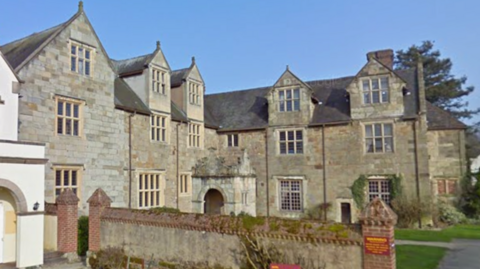 A three storey brick building with large windows and a sloped grey roof