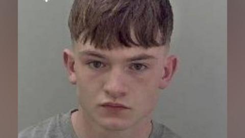 A mugshot of Alex Quinn, who is a young-looking man with short brown hair wearing a grey T-shirt.