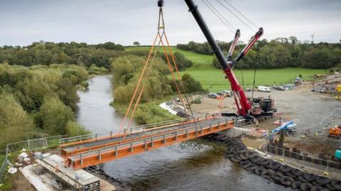 The installation of the new 124 tonne temporary bridge that will provide access over the River Caldew to contractors