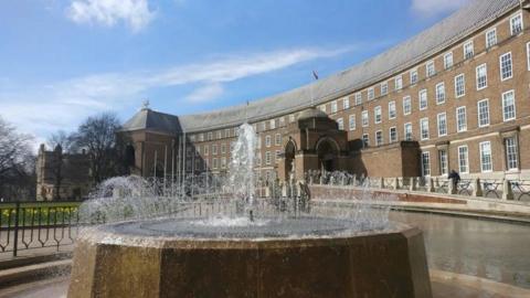 Bristol City Council HQ. It is a wide, brick building with lots of windows. There is a fountain in front of it.