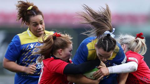Bryonie King of Gwalia Lightning is tackled by Niamh Terry and Meg Webb of Brython Thunder 