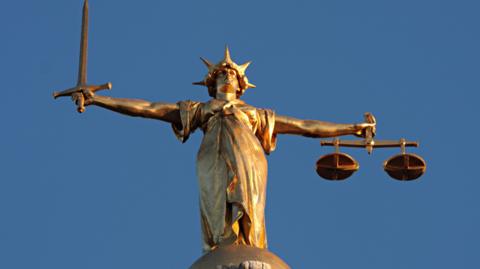 A figure of Lady Justice in gold, seen against a blue sky.