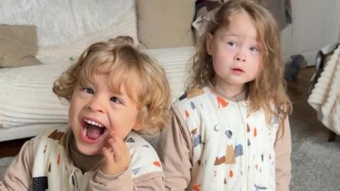 Two small children in patterned onesies. Harry on the left grinning for the camera and Harley on the right looking towards the camera.
