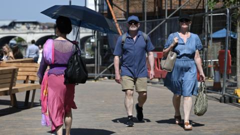 People wearing caps or holding an umbrella walk in the heat in London