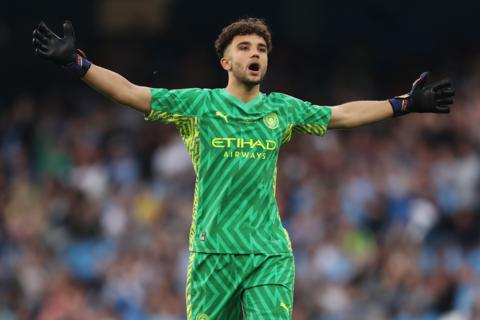True Grant wears a green patterned Manchester City kit and holds his arms out widespread whilst exclaiming