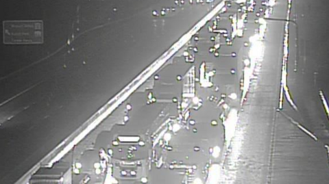 A black and white image of traffic, including both cars and lorries, queuing across multiple lanes on a motorway.