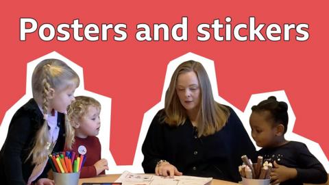 An early years specialist and three young children fill in a poster that is all about them. 