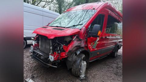 A picture of a red van which has been mangled up and dumped on a muddy car park. 