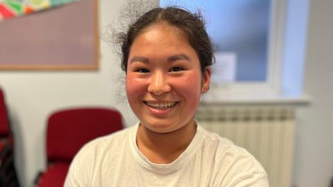 A girl with messy black hair smiling at camera. 