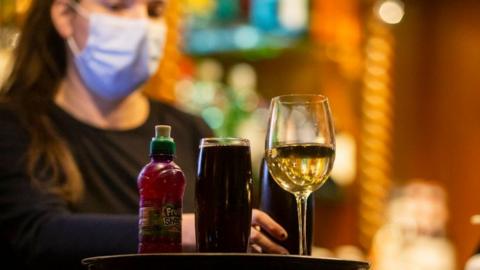 A bar worker serves a mixture of alcoholic and non alcoholic drinks