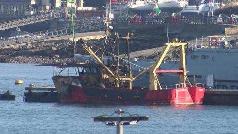 A red boat is partially burnt with black marks along the hull. 