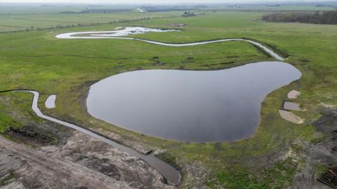 An aerial view of a flat landscape with a large pond in the centre and other rivulets nearby.